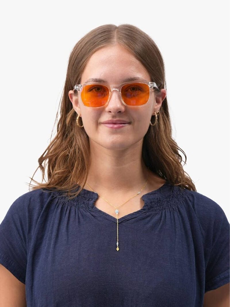 Kvinna med klar båge och orange glasögon, guldörhängen och kedjehalsband, mörkblå topp