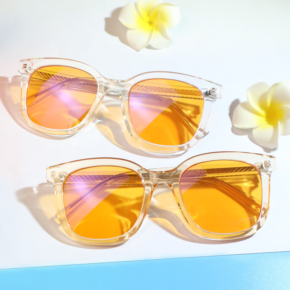 Två solglasögon med genomskinliga bågar och orange spegelglas på vit bakgrund med plumeria-blommor