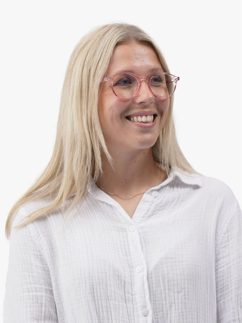 Leende kvinna med långt ljusblont hår, genomskinliga rosa glasögon och vit knäppbar blus