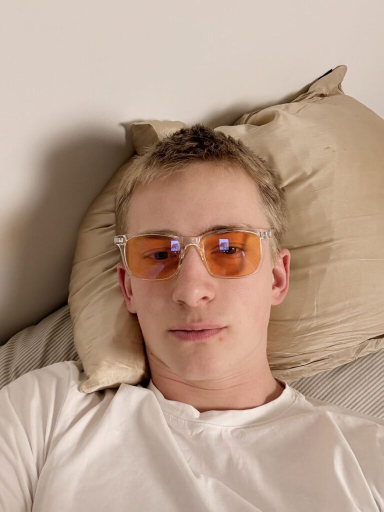 Person som ligger på kudde i vit t-shirt och bär orangefärgade blåljusglasögon